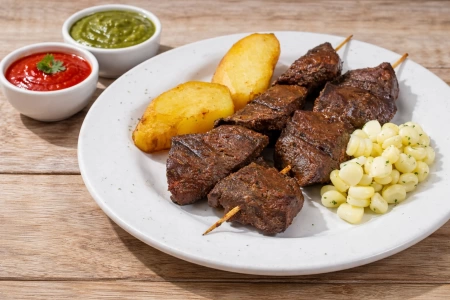 Anticuchos de corazón de vaca con papas doradas y choclo