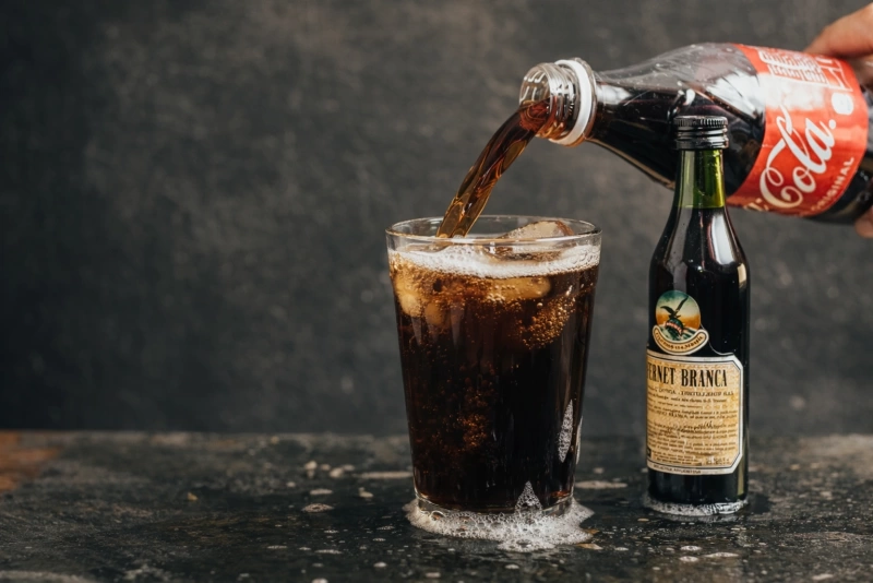 Vaso de fernet con coca y hielo en una mesa de madera
