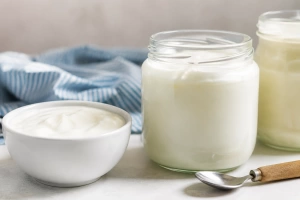 Frasco de vidrio con yogur cremoso y cuchara con mango de madera al lado