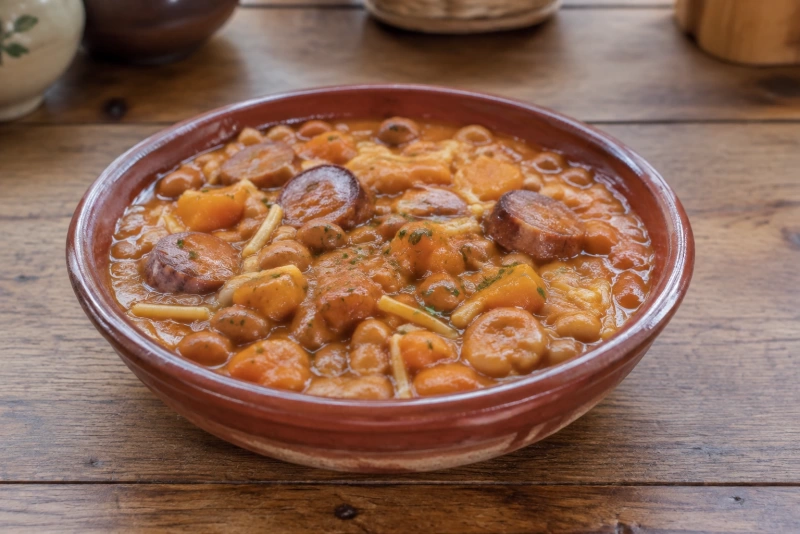 Un plato humeante de porotos con fideos y longaniza cilantro encima