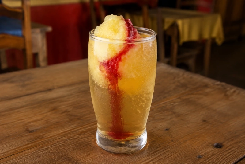 Vaso grande de terremoto chileno con helado de piña vino pipeño y granadina colorida